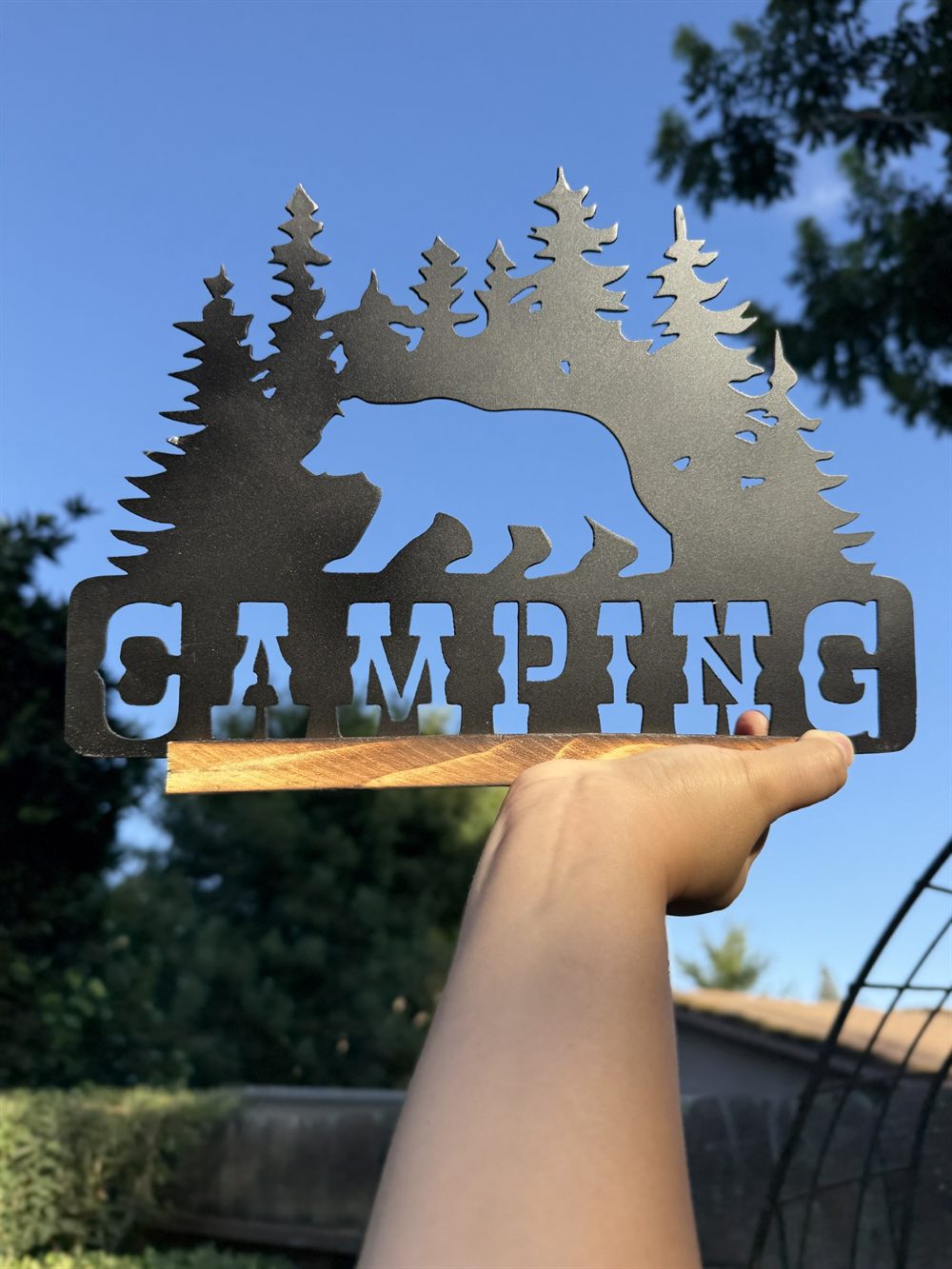 A bear and pine trees above the word Camping, cut from steel.